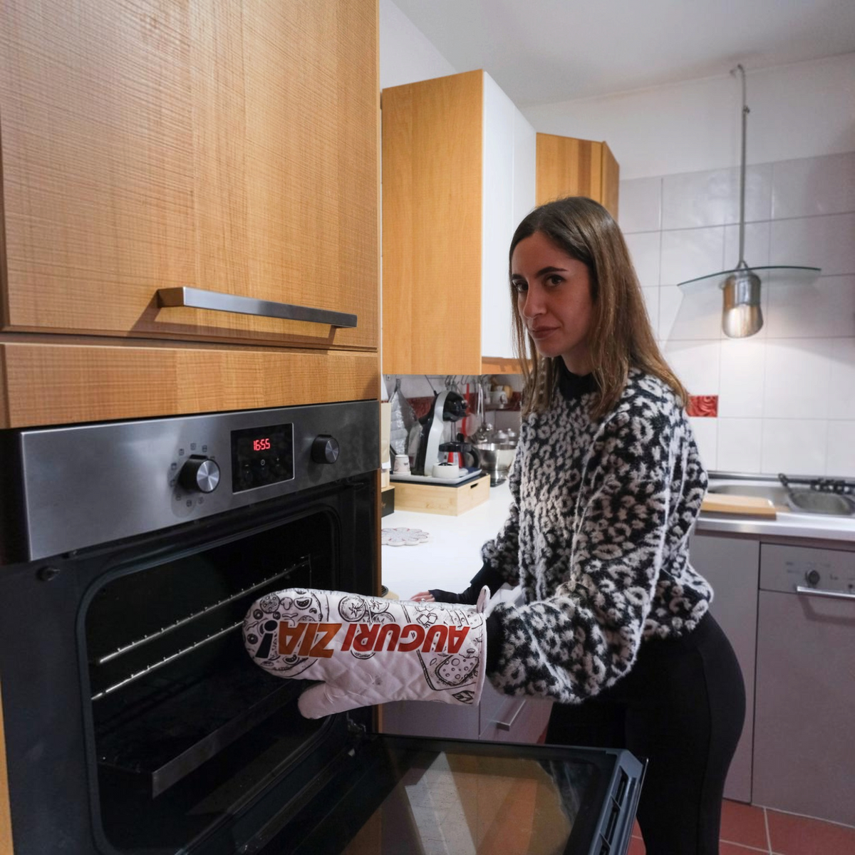Donna indossa un guanto da forno personalizzato FotoGrafica con scritta Auguri Zia davanti a un forno in cucina