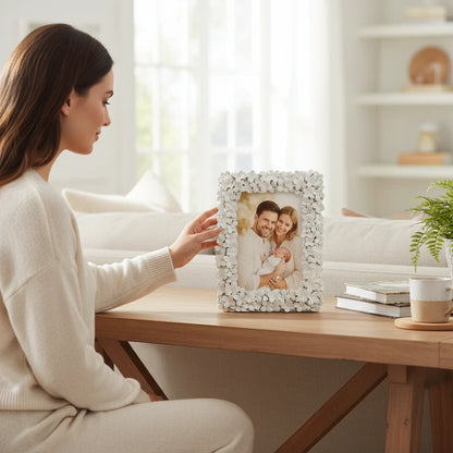 Donna che posiziona una cornice portafoto da tavolo FotoGrafica bianca con decorazioni floreali su un tavolo in legno