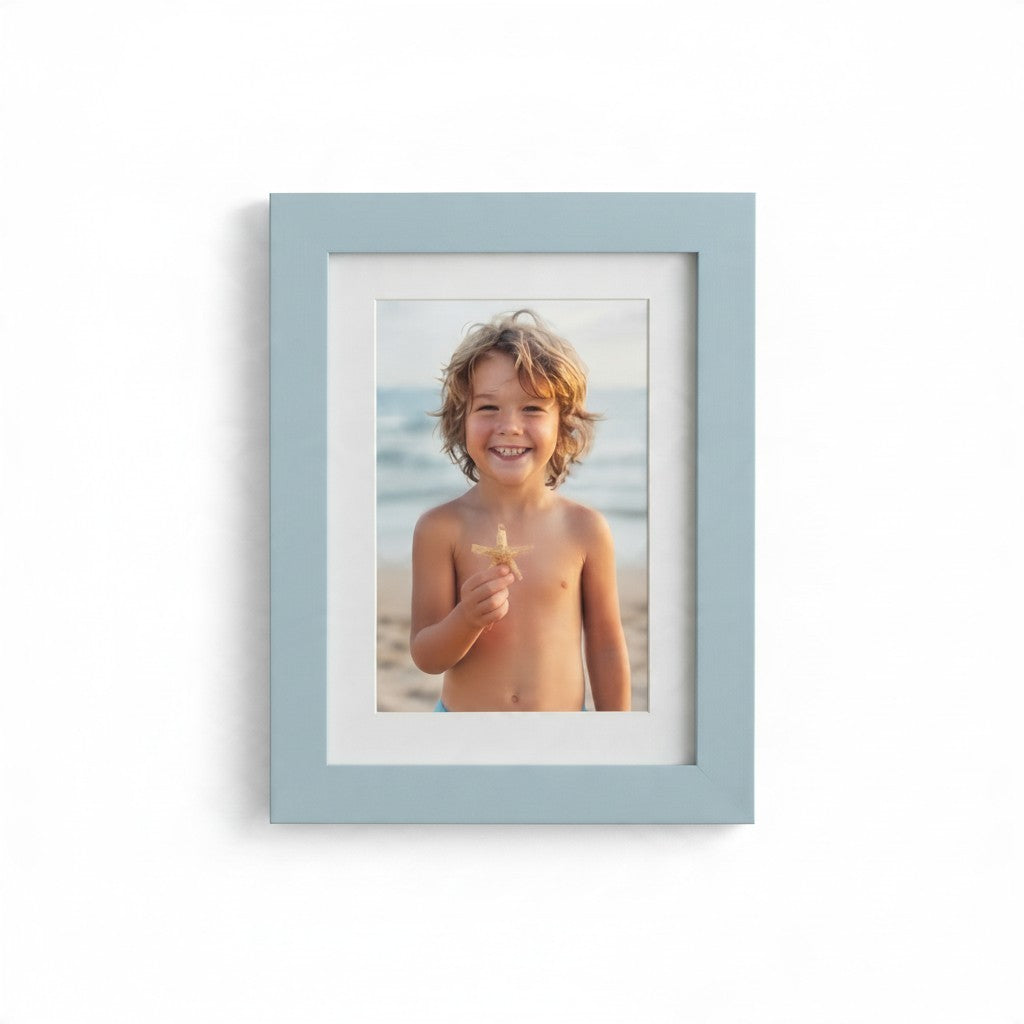 Cornice ricordo FotoGrafica azzurra con passepartout bianco contenente la foto di un bambino sorridente in spiaggia