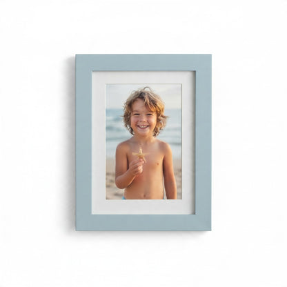 Cornice ricordo FotoGrafica azzurra con passepartout bianco contenente la foto di un bambino sorridente in spiaggia
